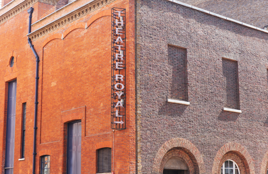 Photograph of a historic building with a white façade and large windows on the lower floors, adjacent to a brick structure with decorative circular motifs around the windows. The sky is clear and blu